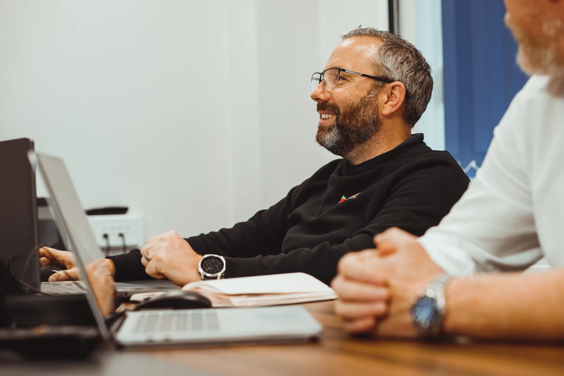 Office staff collaborating at a desk, smiling while working on a laptop.